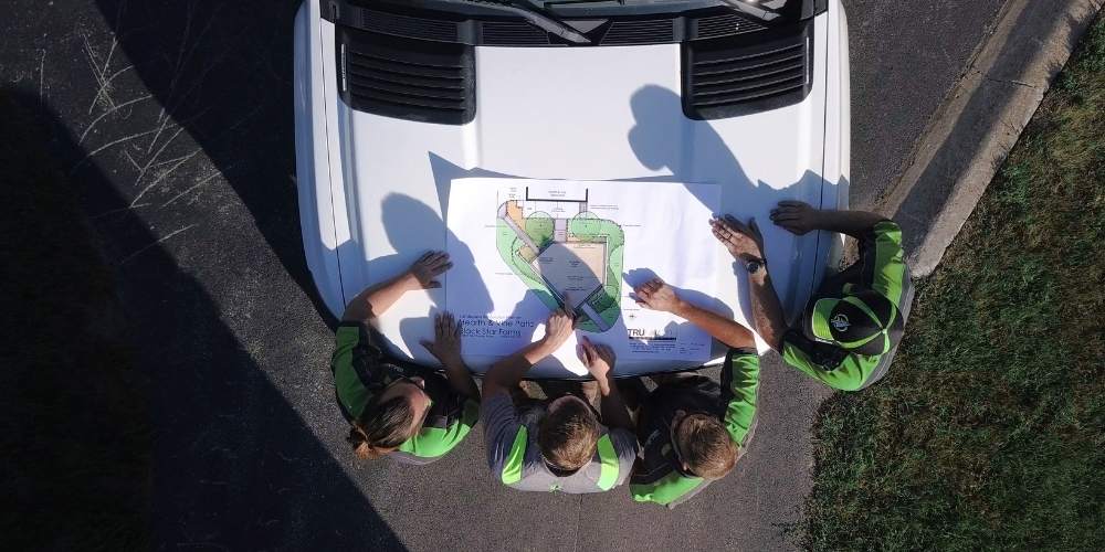 landscape team looks at plan on hood of truck