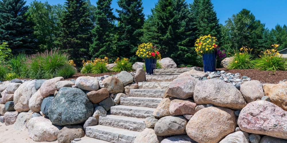 container gardens and grasses near stone steps and boulder retaining wall